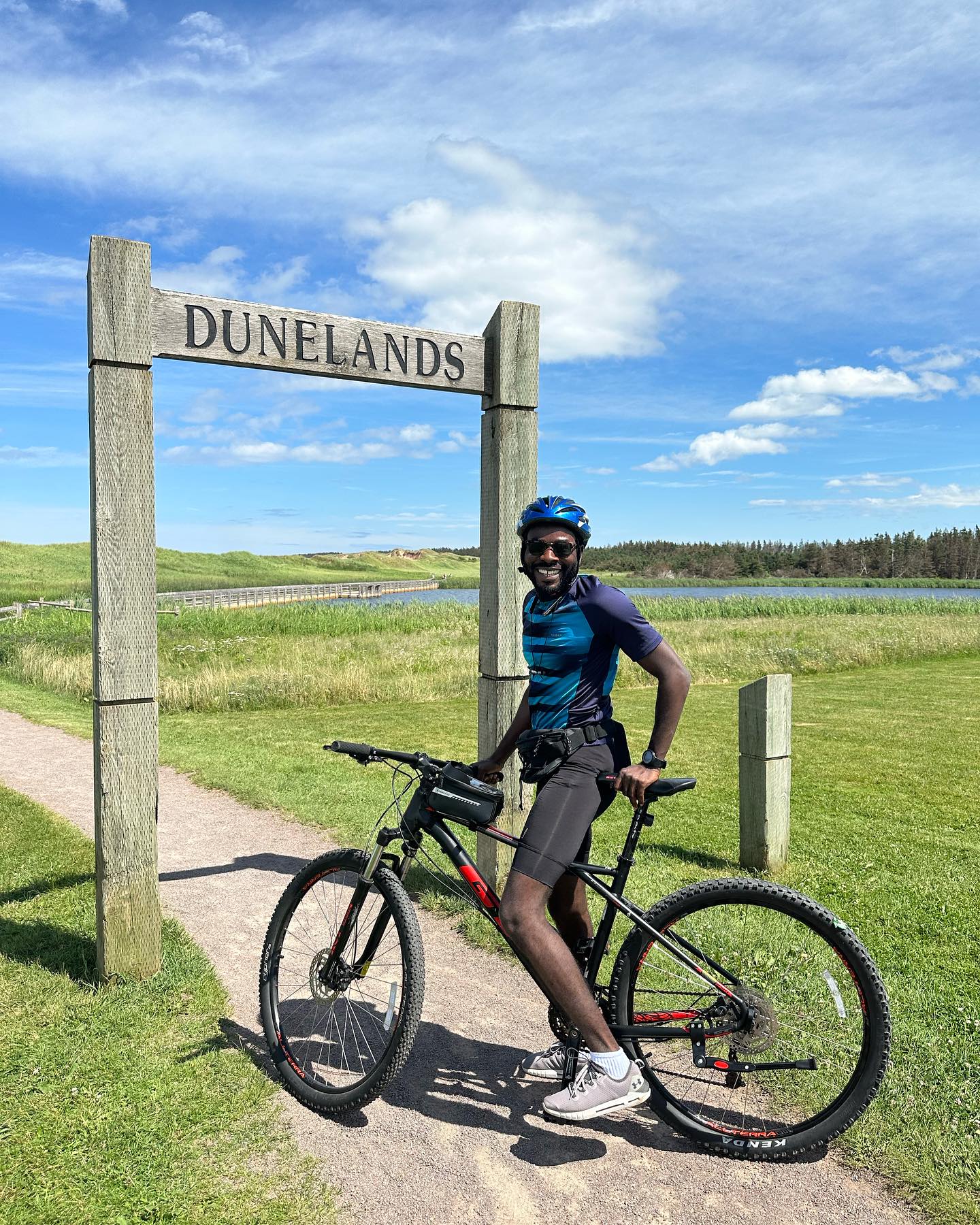 Prosper Habada wearing a cycling helmet beside his bicycle and the Dunelands sign